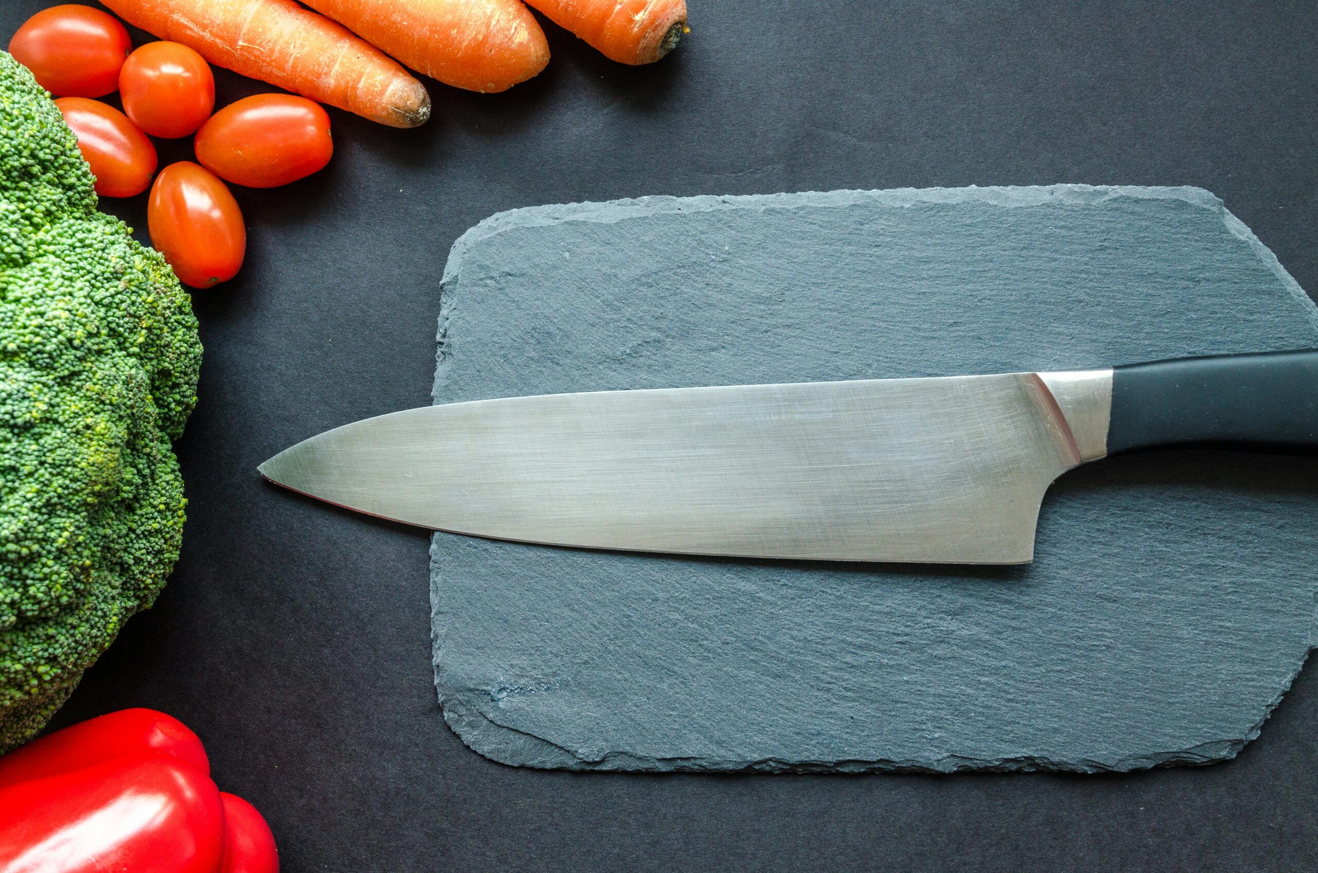 Close-up of fresh vegetables with a chef's knife on a rustic slate board.